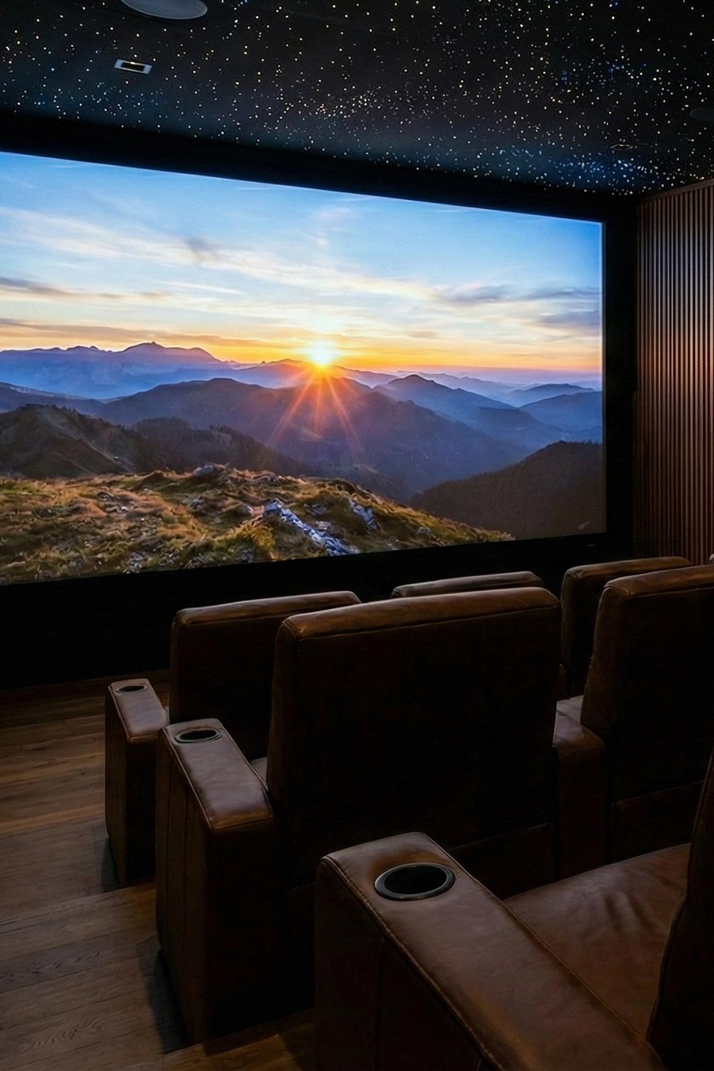 Home theater with brown leather recliners facing a large screen showing a mountain sunrise