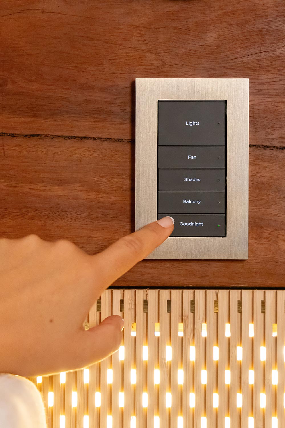 Finger pressing the goodnight button on a sleek metal smart wall switch