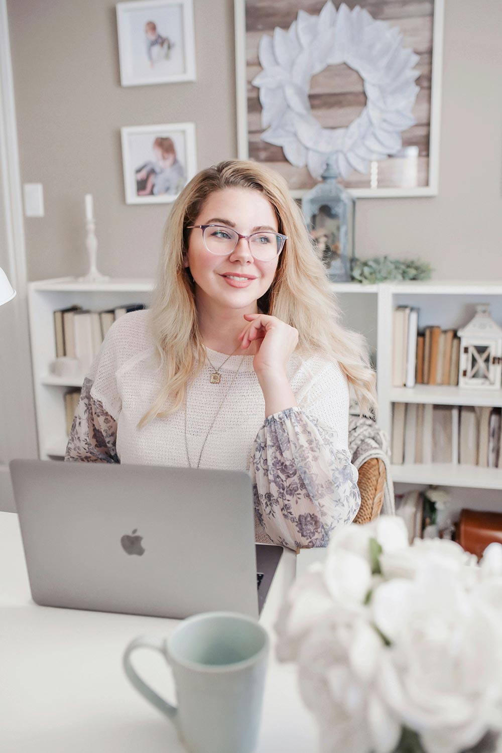 Woman with glasses sitting at a white desk with a silver laptop in a home office