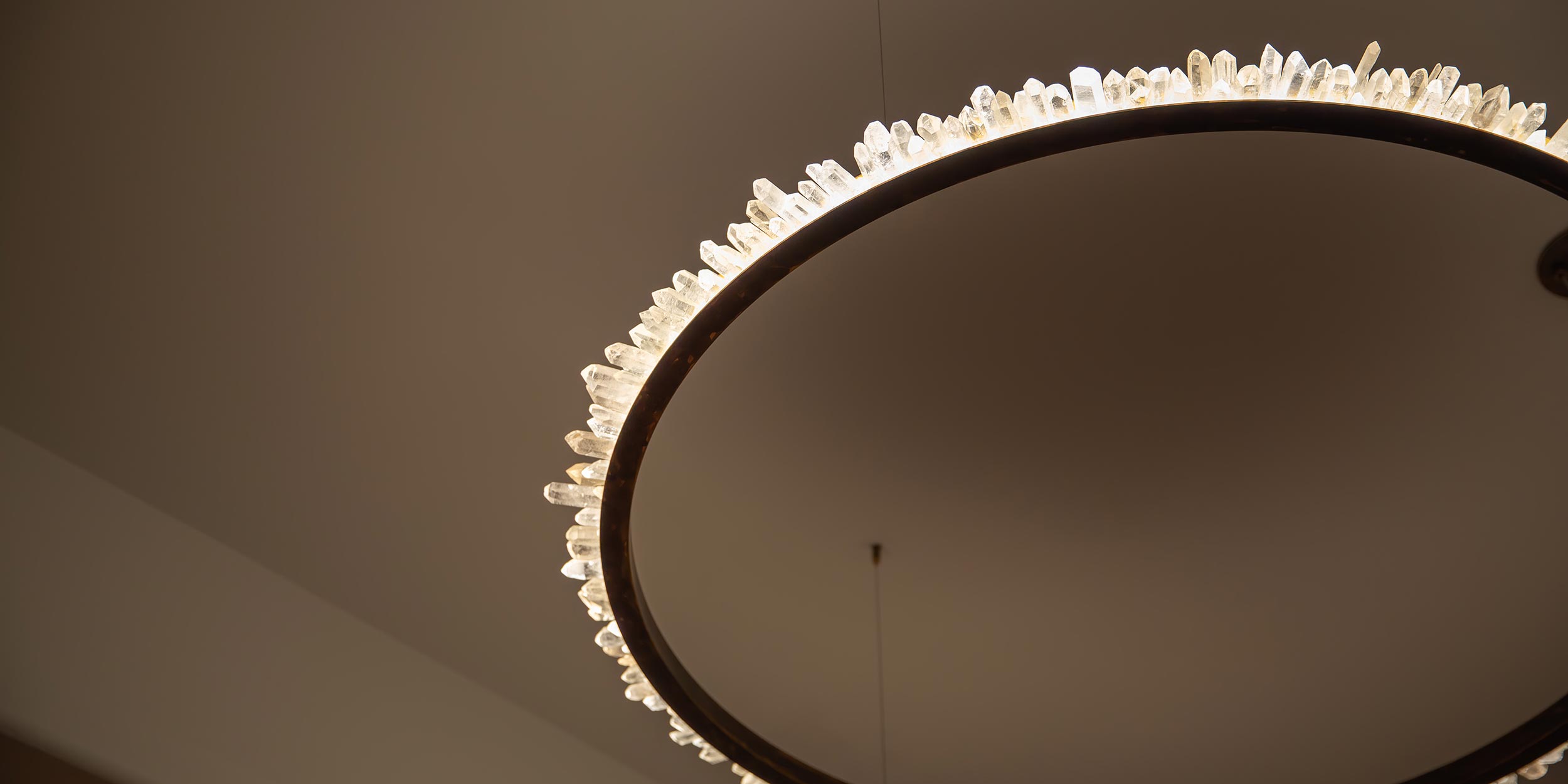 Circular chandelier featuring illuminated raw quartz crystals against a plain ceiling