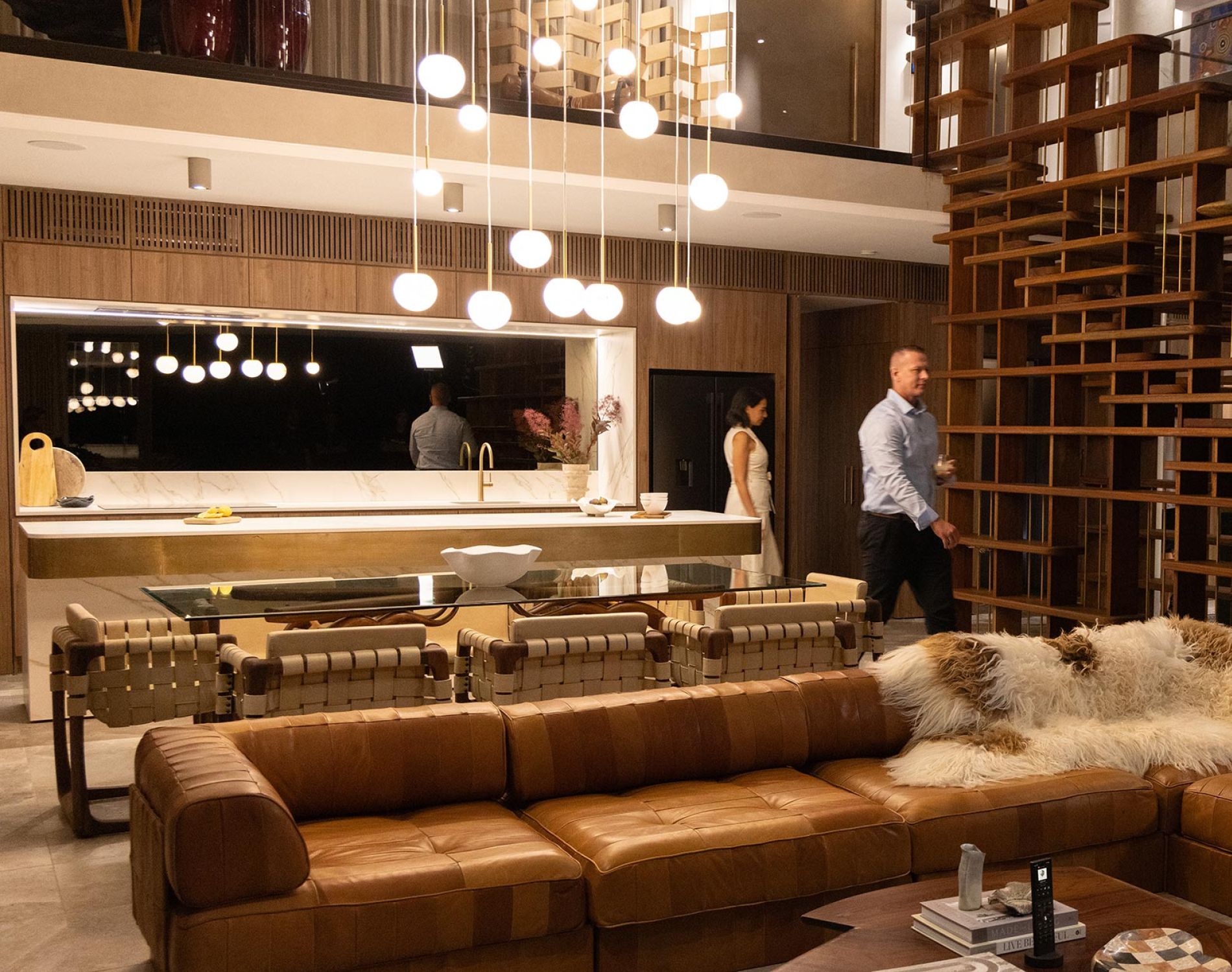 Spacious living area with leather sofa, wooden room divider, and people near a kitchen