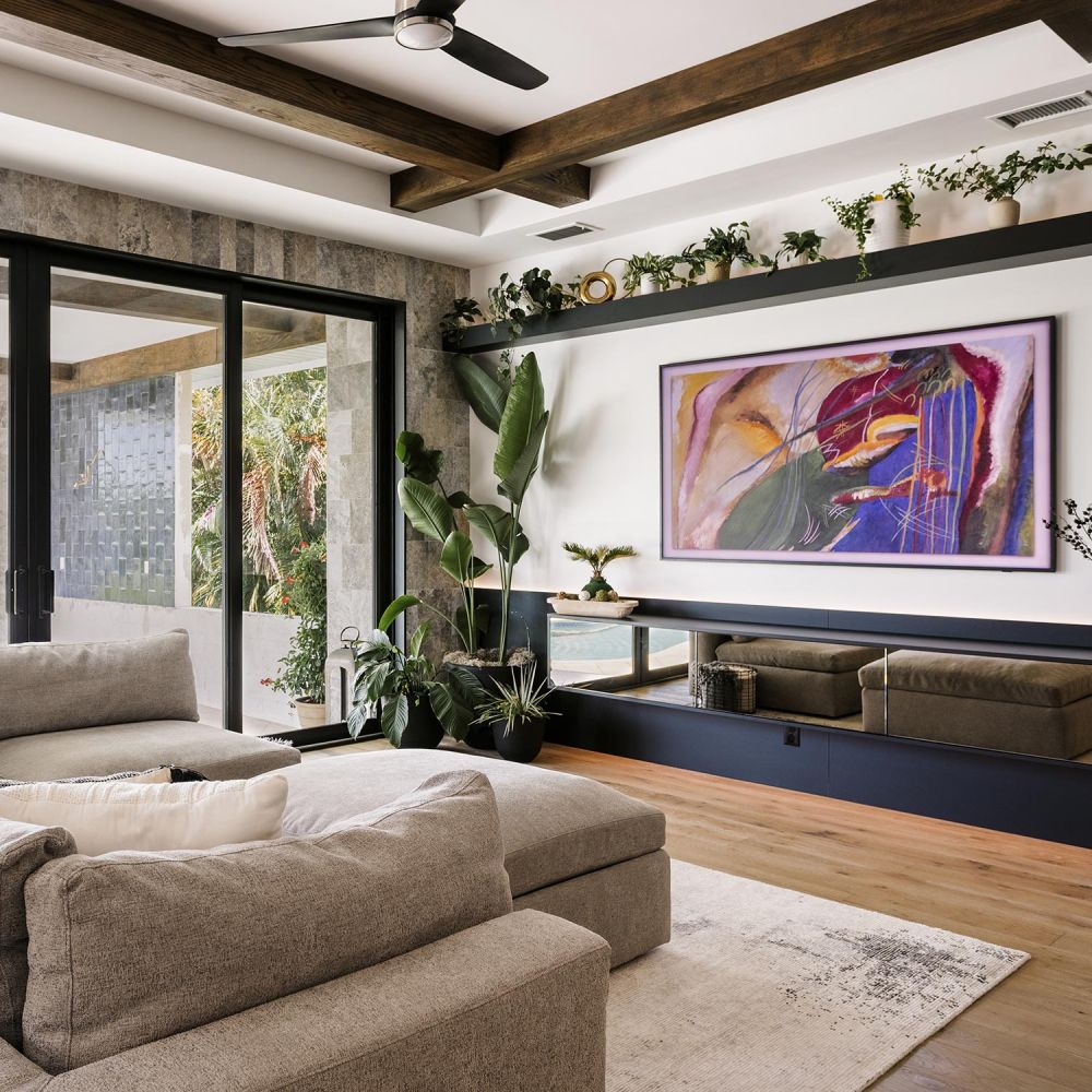 Beige sectional sofa in a bright living room with large potted plants and colorful wall art